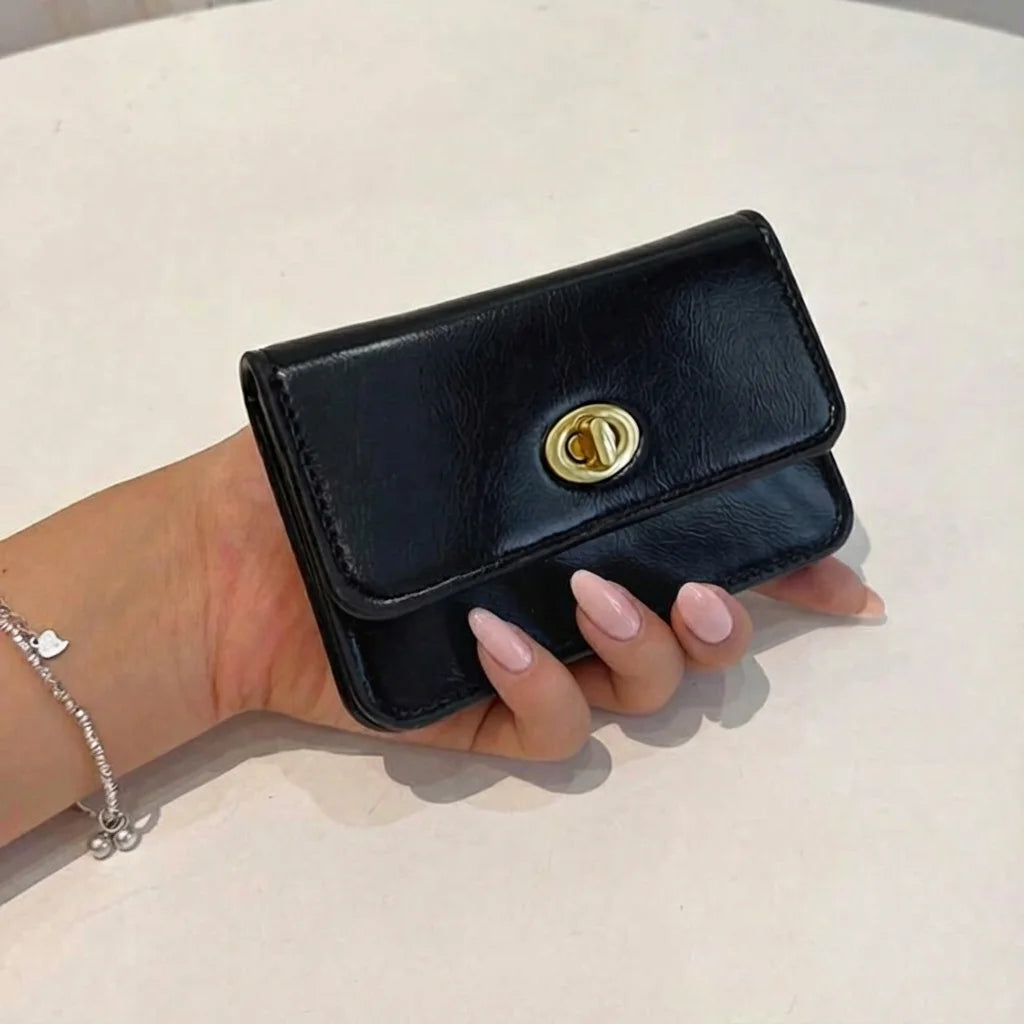 Hand holding a black wallet with a gold clasp on a light background