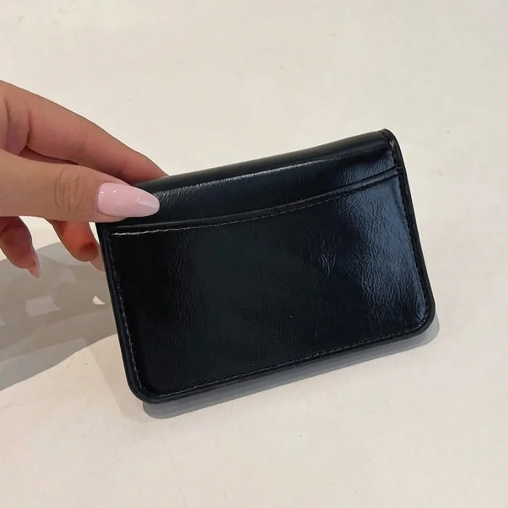 Black wallet held by a hand with pink nail polish on a light background