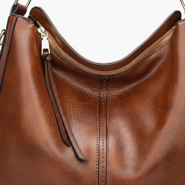 Close-up of brown vegan leather shoulder bag with gold zipper detailing and shoulder strap accents