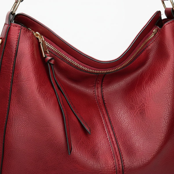 Close-up of red vegan leather shoulder bag with gold zipper detailing and shoulder strap accents