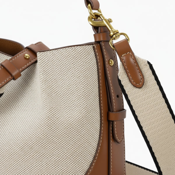 Calypso Vegan Leather Crossbody Bag in beige, closeup highlighting textured canvas, brown vegan leather edges, and gold swivel clasps