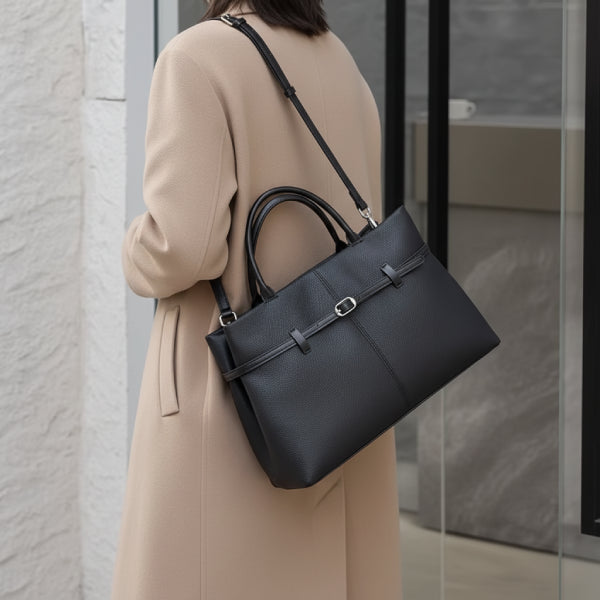 Side view of a woman carrying a sleek black genuine leather tote bag with adjustable shoulder straps, paired with a beige coat