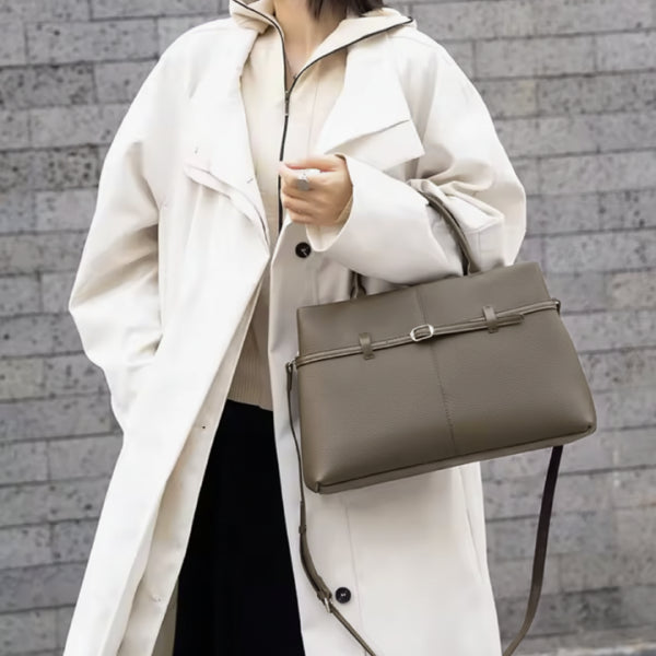 Side view of a woman wearing a white coat and holding a stylish khaki genuine leather tote bag with buckle detailing and adjustable shoulder strap