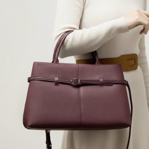 Side view of a woman holding a stylish wine red genuine leather tote bag, featuring elegant buckle detailing and a detachable shoulder strap