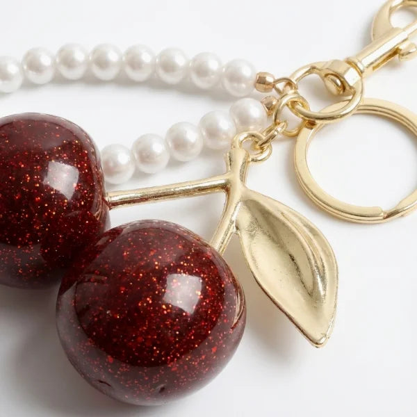 Keychain with red cherry and gold leaf charm on a white background