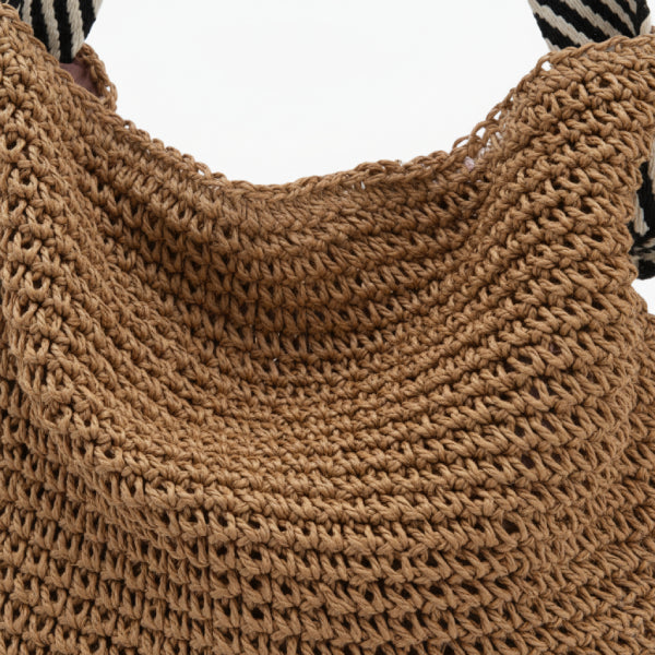 Close-up of brown woven tote bag with textured material and striped black and white handles, showcasing the craftsmanship