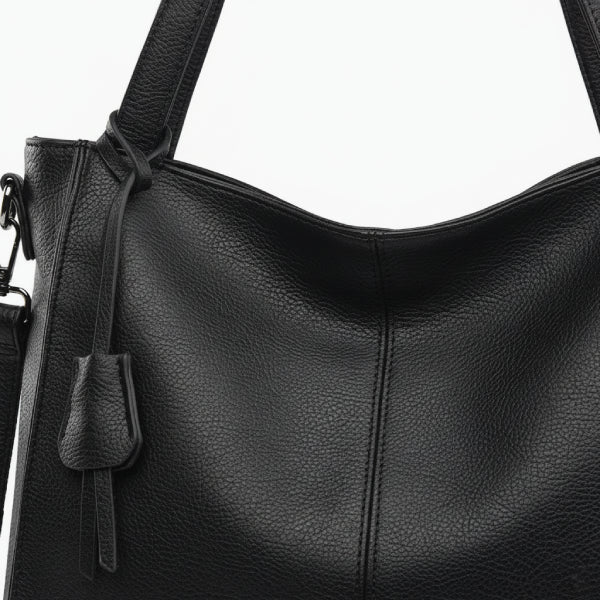 Close-up of the black vegan leather tote bag featuring a smooth texture, long straps, and a decorative leather tassel