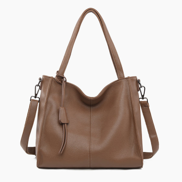 Front view of a brown vegan leather tote bag featuring a minimalist design with a central tassel detail and elegant handles