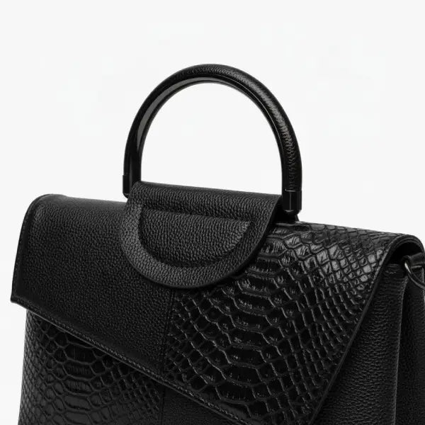 Close-up of a black vegan leather satchel bag featuring a geometric design with a croc-embossed flap and top handle