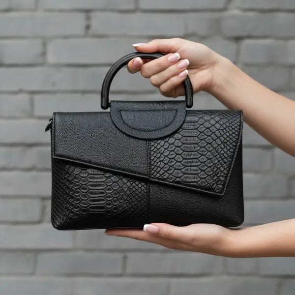 Model holding a black vegan leather satchel bag with a croc-embossed flap in a casual outdoor setting