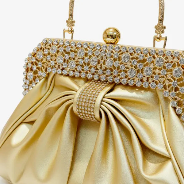 Close-up of a gold vegan leather evening bag featuring rhinestone detailing on the gold frame and pleated satin fabric