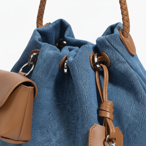 Evelisse Denim Bucket Bag in denim blue, closeup of drawstring eyelets, braided handle attachment, and tan leather accents