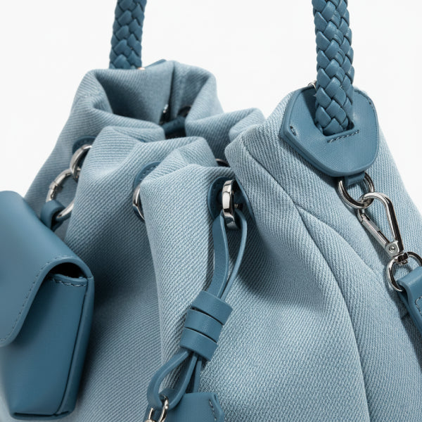 Evelisse Denim Bucket Bag in light blue, closeup of drawstring eyelets, braided handle attachments, and matching leather accents