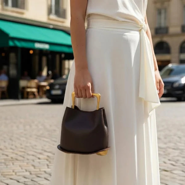 Person holding a Coffee Izelia top grain leather crossbody bag with gold handle on a city street