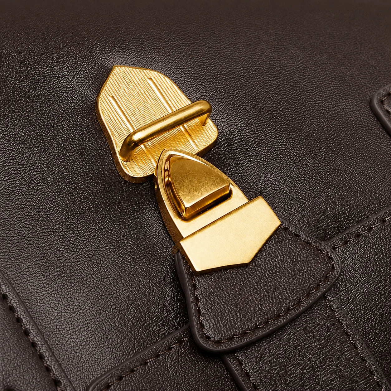 Close-up of a black textured leather bag featuring a prominent gold-tone metal clasp and strap attachment.