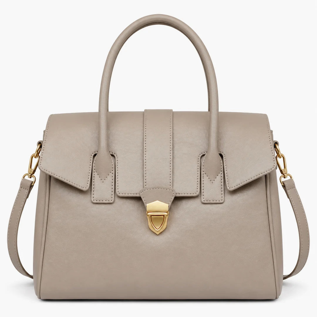 A structured taupe leather handbag with dual top handles, a front flap closure, and a gold-tone shield-shaped clasp, shown on a plain white background.