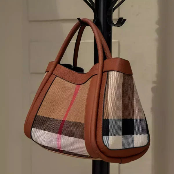 Plaid handbag with brown leather accents hanging on a black coat rack.