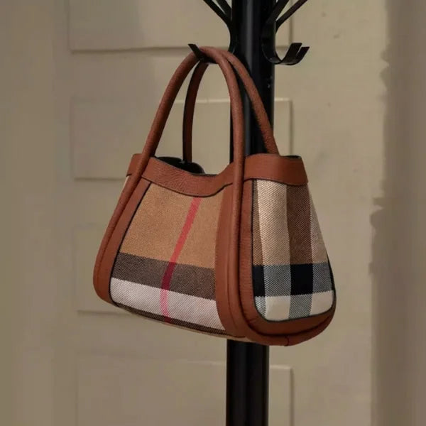 Plaid handbag with brown leather accents hanging on a black coat rack.