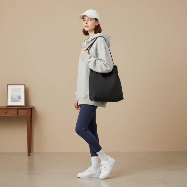 Model wearing a gray hoodie and leggings, carrying the black Marinda corduroy tote bag in a minimalist indoor setting