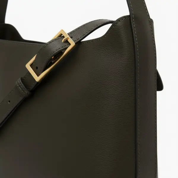 Close-up of black vegan leather shoulder bag with gold buckle detail on strap and sleek design