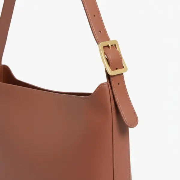 Close-up of brown vegan leather shoulder bag with gold buckle detailing on the strap and smooth texture