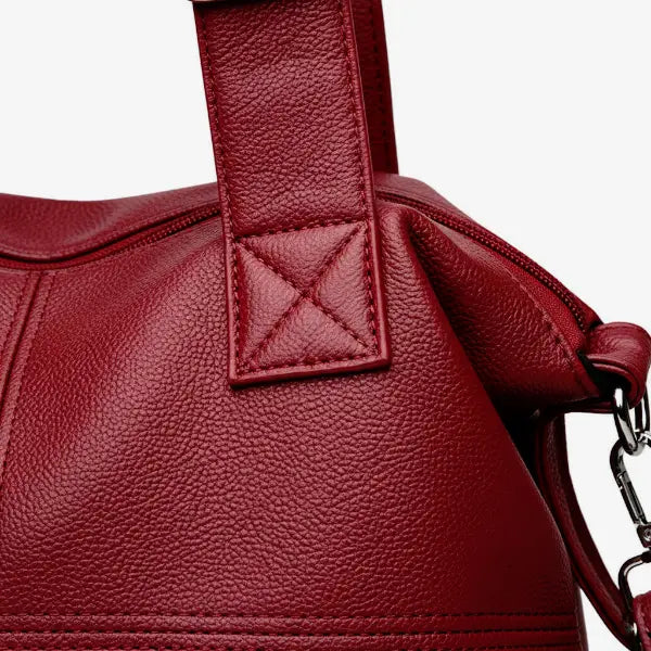 Close-up of Mirelith red leather satchel bag with quilted handles and adjustable strap with silver hardware