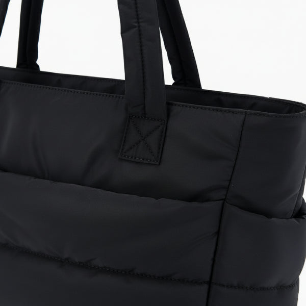 Close-up of black puffer-style tote bag with quilted texture and sturdy handles for a stylish, modern look