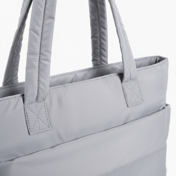 Close-up of grey puffer-style tote bag, focusing on its soft, quilted material and sturdy handles for a minimalist look