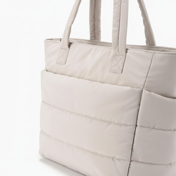 Close-up of off-white puffer-style tote bag with quilted design and sturdy handles, exuding a minimalist chic vibe