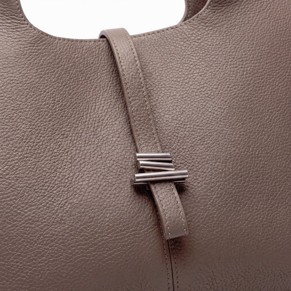 Close-up of a taupe pebbled leather handbag featuring a vertical strap with a polished silver-toned geometric metal clasp.