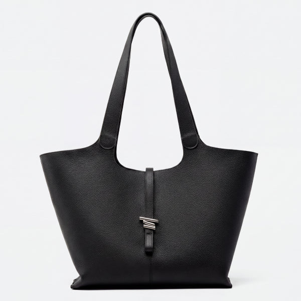 A black pebbled leather tote bag with dual shoulder straps and a central vertical strap featuring a silver-toned geometric logo clasp, shown against a plain white background.