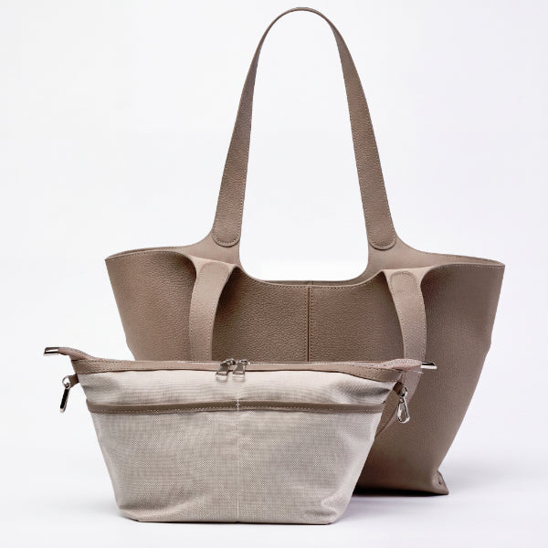 A taupe leather tote bag with dual shoulder straps and a matching zippered pouch in a light beige textured fabric, displayed against a clean white background.
