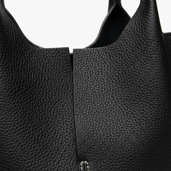 Close-up of black cowhide leather tote bag, showcasing its textured leather and minimalist design with contrasting white stitching