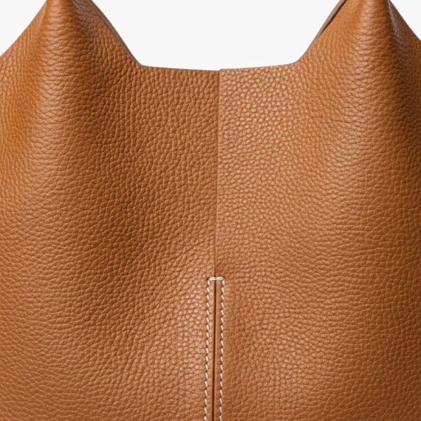 Close-up of caramel cowhide leather tote bag, highlighting the textured leather and contrast stitching for a stylish, modern appearance