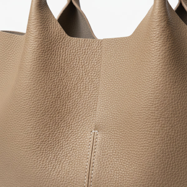 Close-up of khaki cowhide leather tote bag, showcasing its textured leather and central seam with clean white stitching