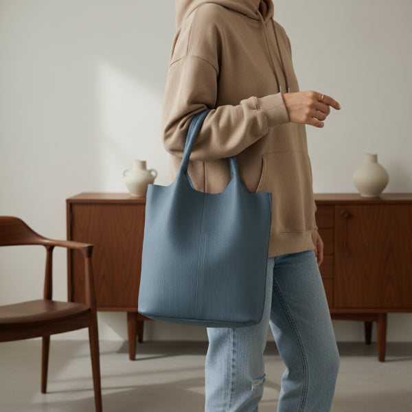 Model carrying blue cowhide leather tote bag with minimalist design, paired with a beige hoodie for a stylish and casual look