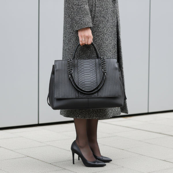 Model carrying a black genuine leather tote bag with chain handles, styled in a fashionable outfit for a sleek, professional appearance