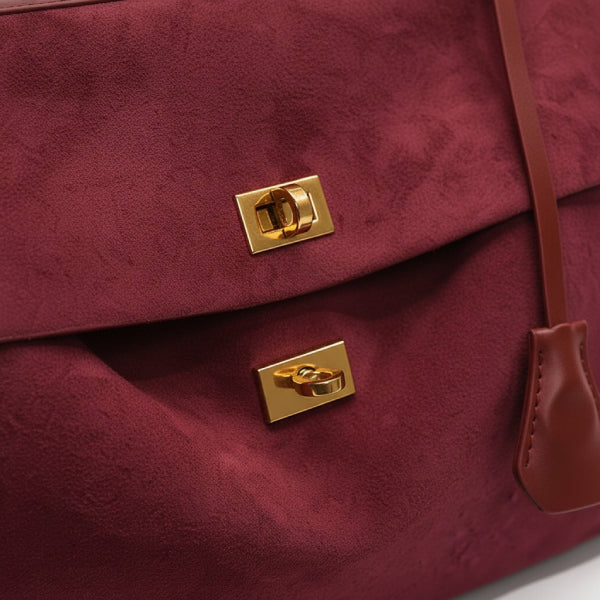 Close-up of red velvet satchel bag with gold metal clasp and lock detailing