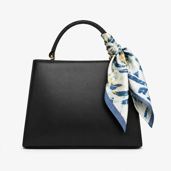 A black leather top-handle handbag with a blue, white, and yellow patterned silk scarf tied to the handle, shown against a plain white background.