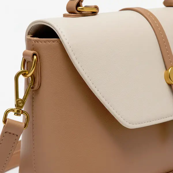 Close-up of a beige vegan leather crossbody bag with gold hardware and a flap closure