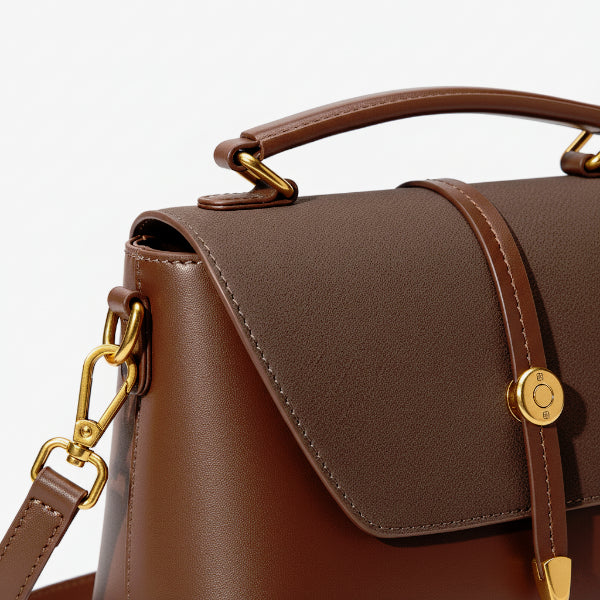 Close-up of a brown vegan leather crossbody bag showing the gold hardware, flap closure, and detailed stitching on the edges