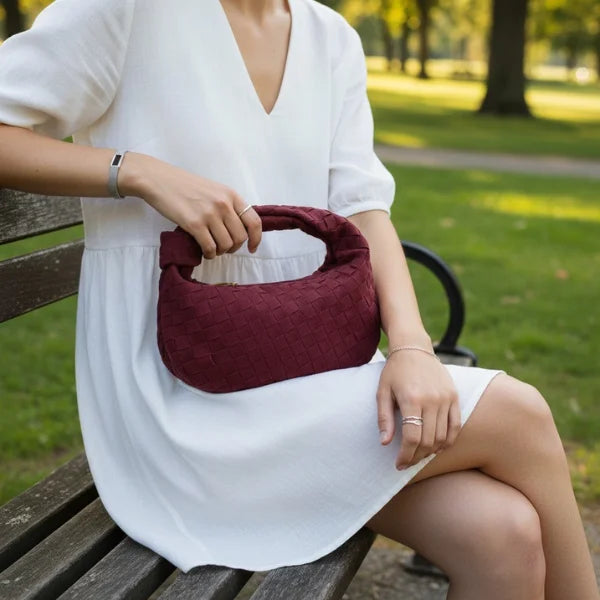 Seraphine Vegan Leather Hobo Bag in wine red, lifestyle park scene with model in white dress holding the mini woven hobo