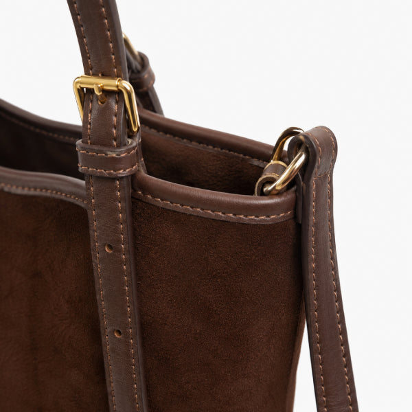 Close-up of a dark brown leather and suede tote bag showing the top edge, strap attachment with gold-tone hardware, and stitching details against a white background.