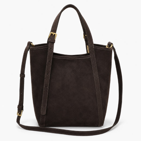 A dark brown suede bucket bag with gold-tone hardware, featuring dual top handles and a detachable shoulder strap, shown against a plain white background.
