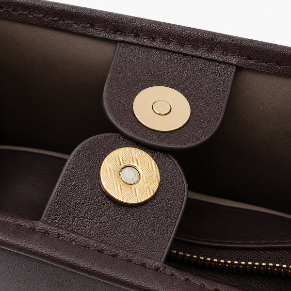Close-up of a dark brown textured leather clutch or handbag interior, showing two gold-tone magnetic snap closures and a zipper.