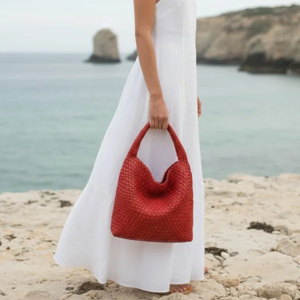 Soraya Vegan Leather Hobo Bag in olive red, coastal lifestyle shot with model holding large woven hobo for chic resort style