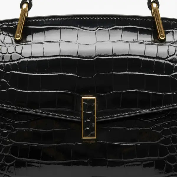 Close-up of black crocodile leather satchel bag with gold rectangular clasp and handle detailing