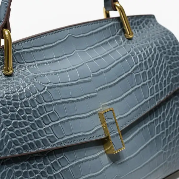 Close-up of blue crocodile leather satchel bag with gold rectangular clasp and handle detailing