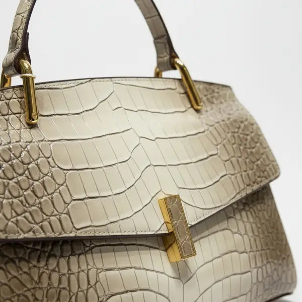 Close-up of gray crocodile leather satchel bag with gold rectangular clasp and handle detailing