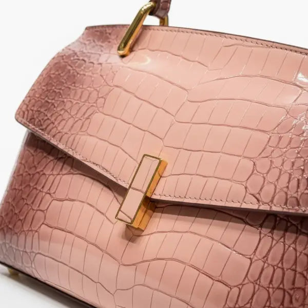 Close-up of pink crocodile leather satchel bag with gold rectangular clasp and handle detailing